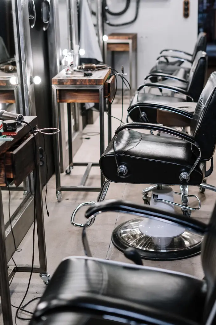 Fila de sillas negras de barbería frente a los espejos