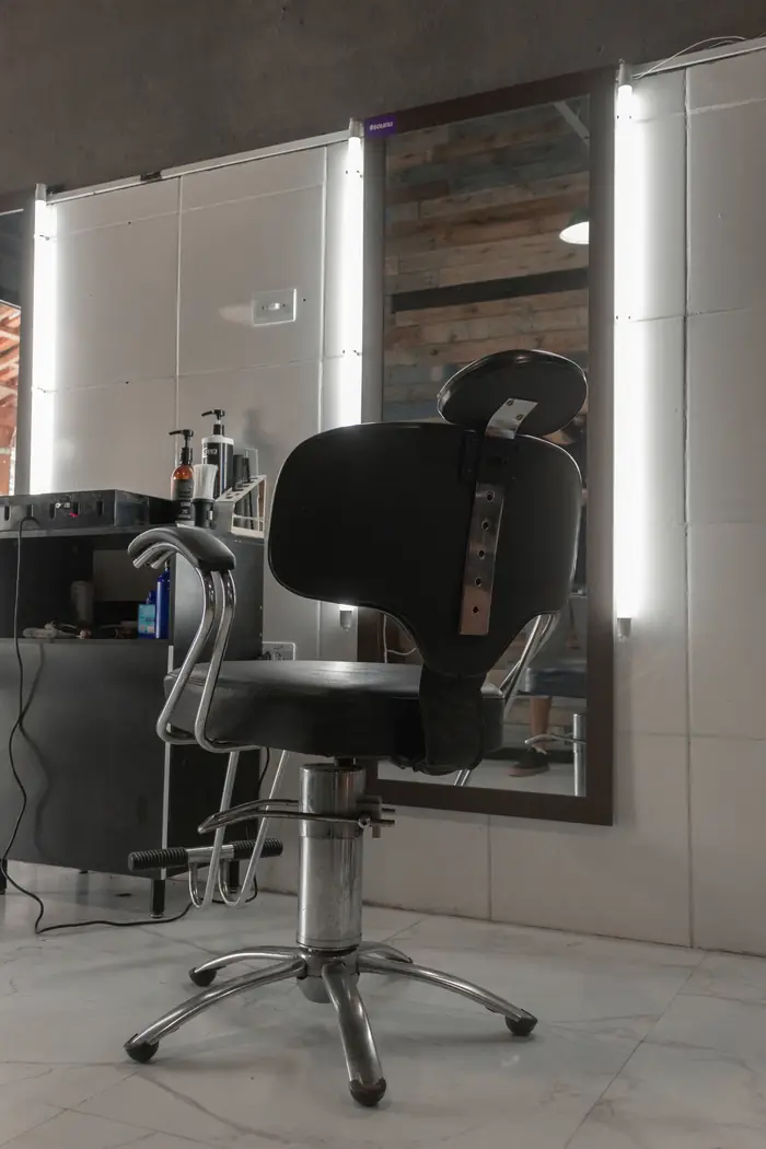 Silla de barbería negra junto a un espejo con luz blanca